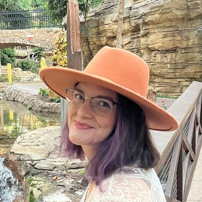 Brianna in an orange wide-brimmed hat beside a garden waterfall