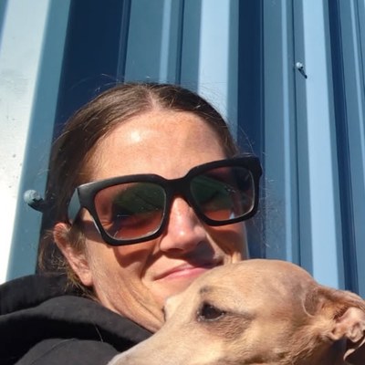 Tisha in sunglasses, cheek to cheek with a tan dog against a blue metal wall